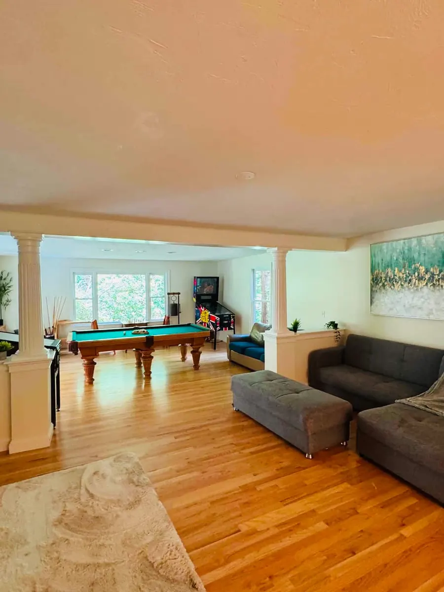 Open living area with sofas, hardwood floors and a pool table beyond