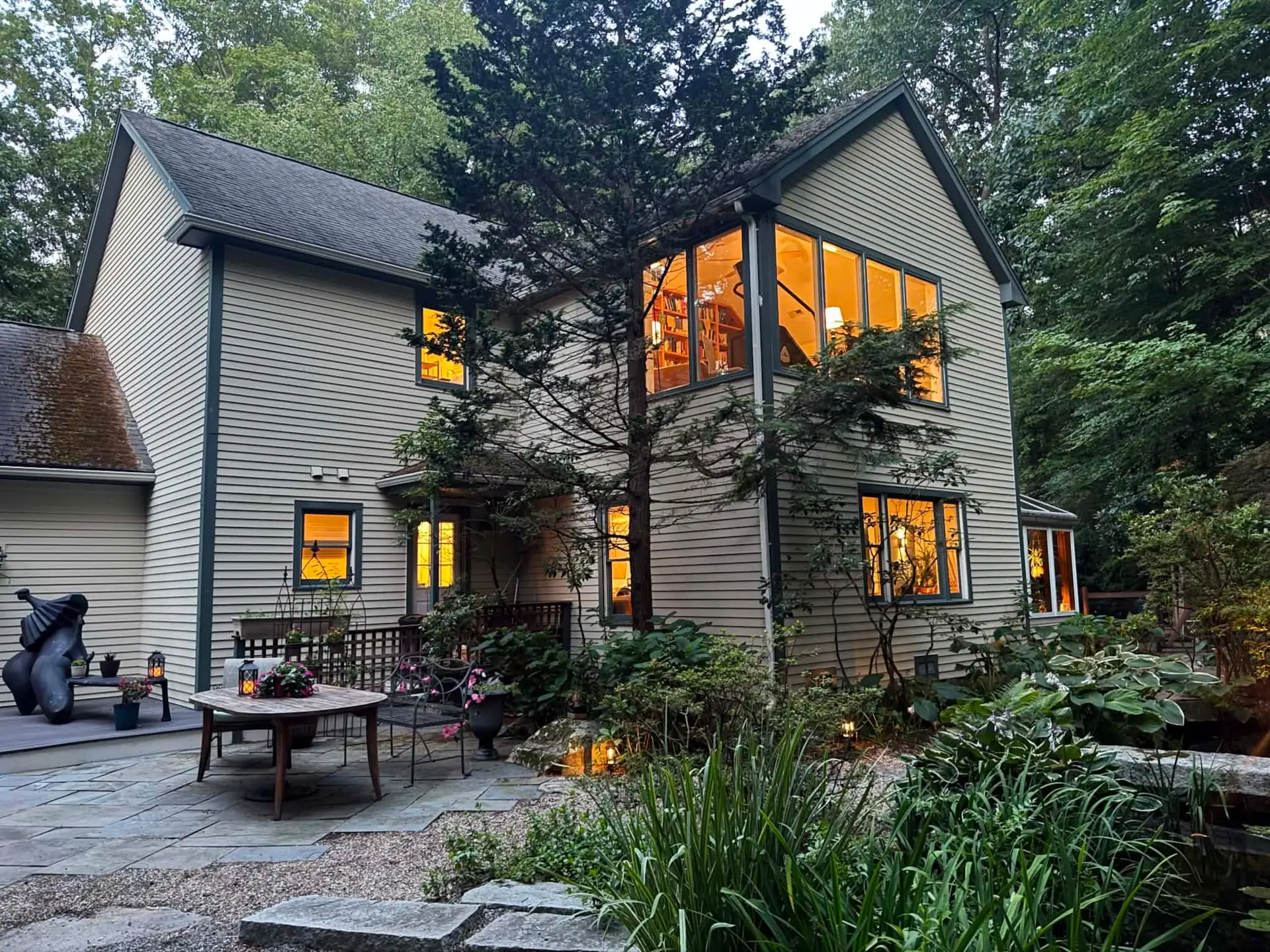 The house at dusk from the garden patio, every window glowing, a table set among the plantings