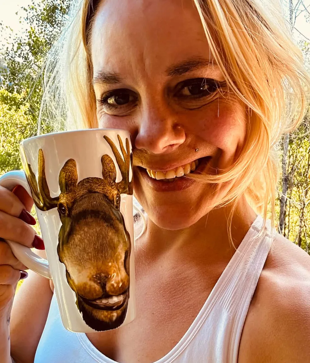 Jillian, your host, smiling on a sunny deck with a tall mug