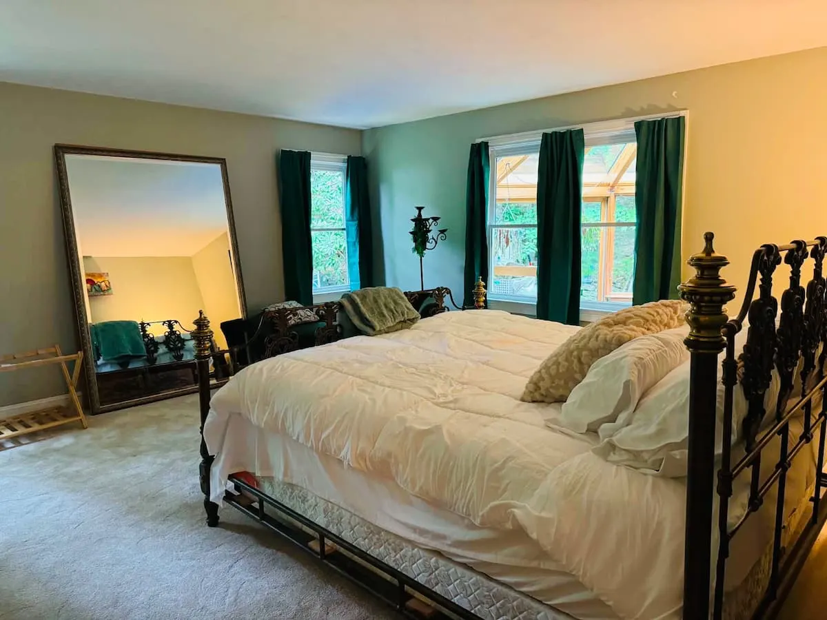 The primary suite with an iron bed frame, a reading chaise and green curtains