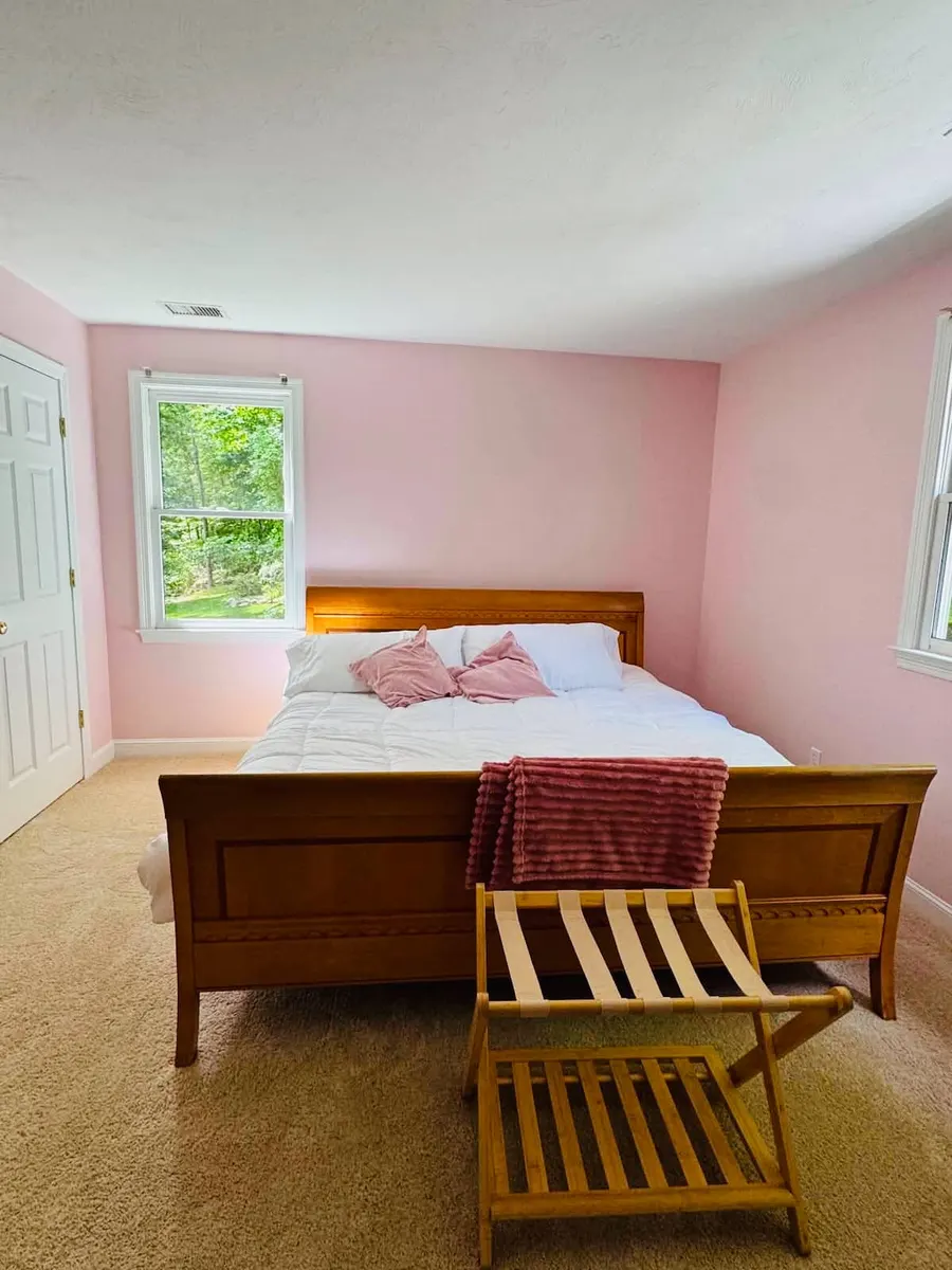 A small bedroom with pink walls, a wooden bed and a luggage rack