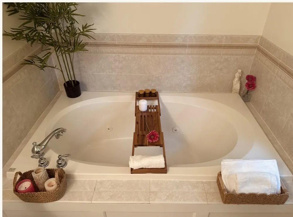 Deep jetted tub with a wooden bath tray, rolled towels and a potted plant